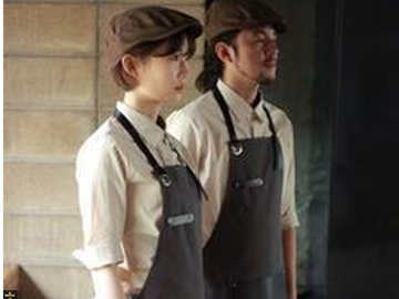 Two individuals wearing aprons and caps in a professional setting