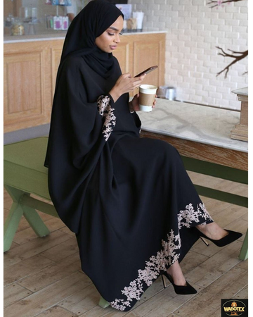Woman in a black abaya with white embroidery sitting on a green chair in a kitchen.