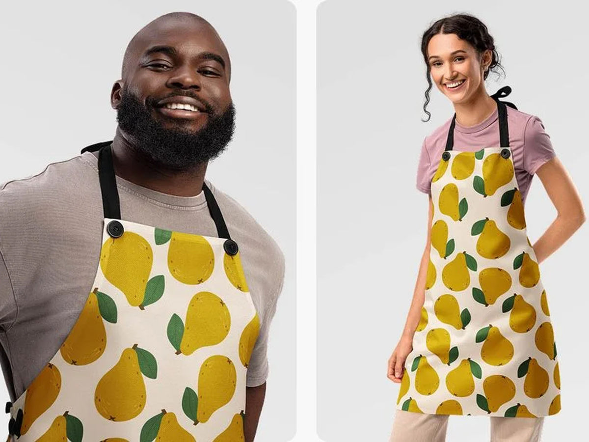 Two models wearing matching aprons with a yellow pear pattern on a cream background. The left model is a smiling man in a gray shirt, and the right model is a woman in a pink shirt.