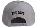 A light gray snapback cap shown from the back, featuring 'EST. 2023' embroidered in black arched lettering on the crown.