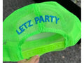 A bright neon green mesh trucker-style cap with blue embroidered text reading 'LETZ PARTY' on the front, held by a hand against an outdoor dark background.