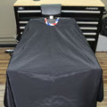 A black horse grooming stall cover draped over a grooming table in front of a Husky tool chest, with a small red, white, and blue ribbon at the top.