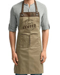 A man wearing a khaki-colored apron with brown leather straps over a gray henley shirt, featuring a printed 'Your Coffee' logo on the chest.