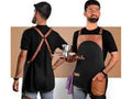 Two people wearing black aprons with brown leather straps against a beige background