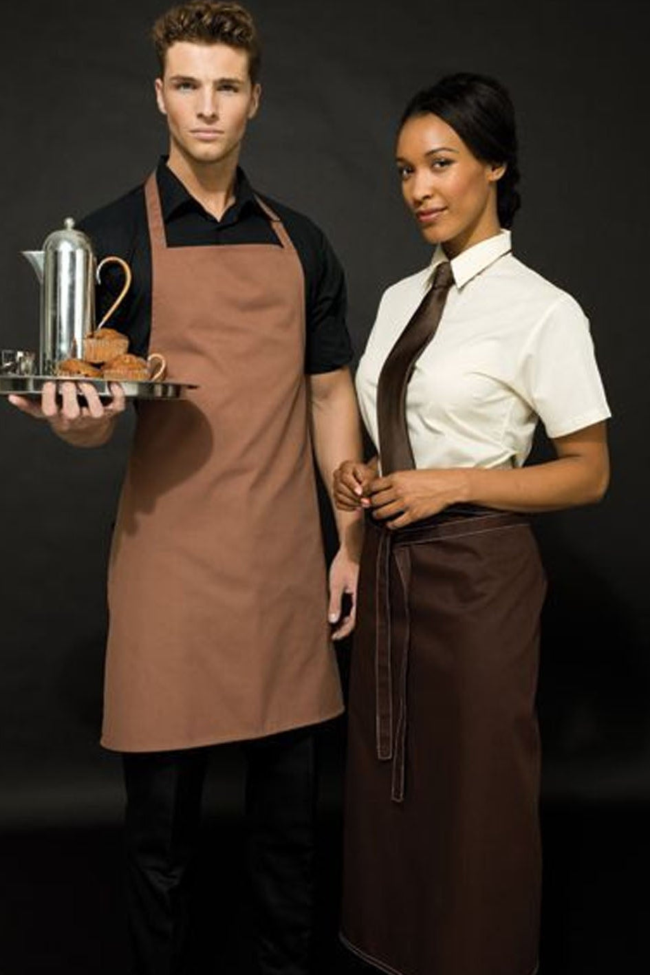 Two waiters in brown aprons standing side by side with a dark background
