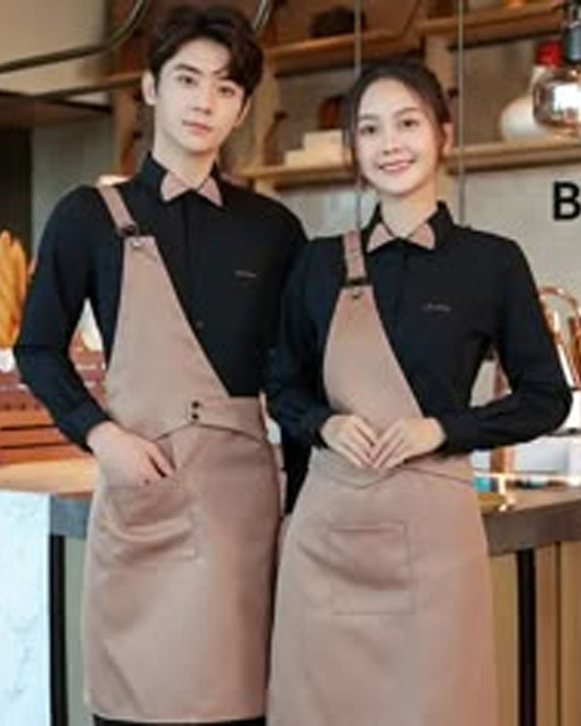Two people wearing matching aprons in a kitchen setting.