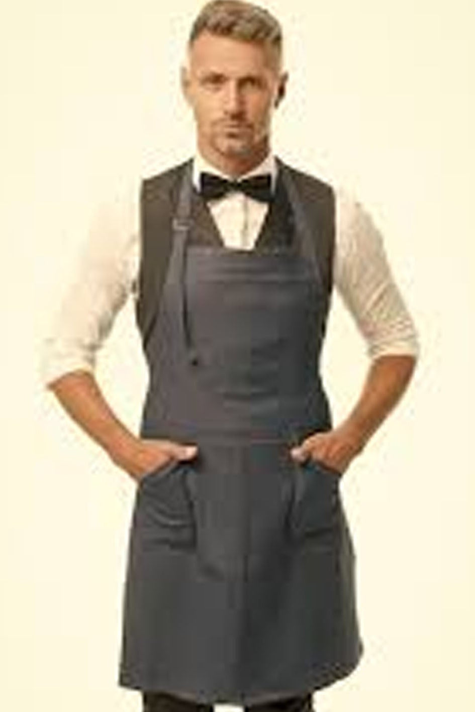 Man wearing a gray apron over a white shirt with a bow tie on a beige background