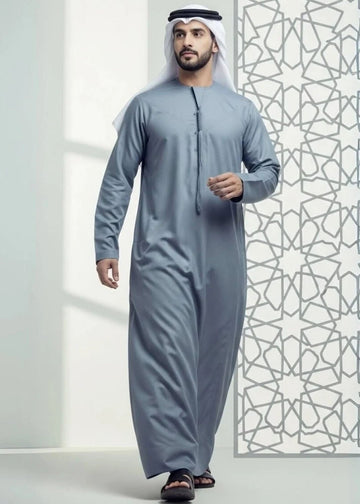 Man wearing a traditional gray outfit with a patterned wall in the background