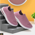 Pink slip-on shoes on a gray surface with a yellow wall and plant in the background