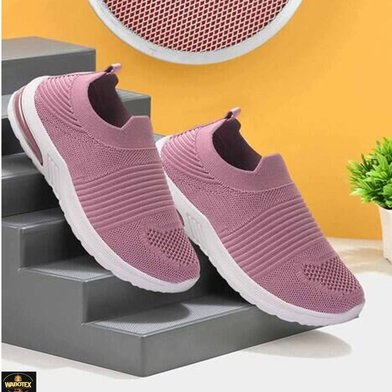 Pink slip-on shoes on a gray surface with a yellow wall and plant in the background