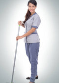 A woman wearing a light gray and blue scrub-style uniform stands holding a long-handled cleaning tool against a plain light gray studio background.