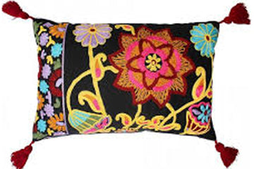 A square decorative throw pillow with a black background and vibrant multicolor floral embroidery, finished with red tassels on the corners, shown against a plain white background.
