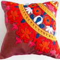 A square decorative throw pillow featuring a vibrant, multicolored hand-embroidered floral pattern on a brown linen-like fabric base, set against a plain white background.