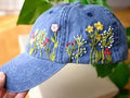 Blue denim cap with floral embroidery held against a blurred natural background