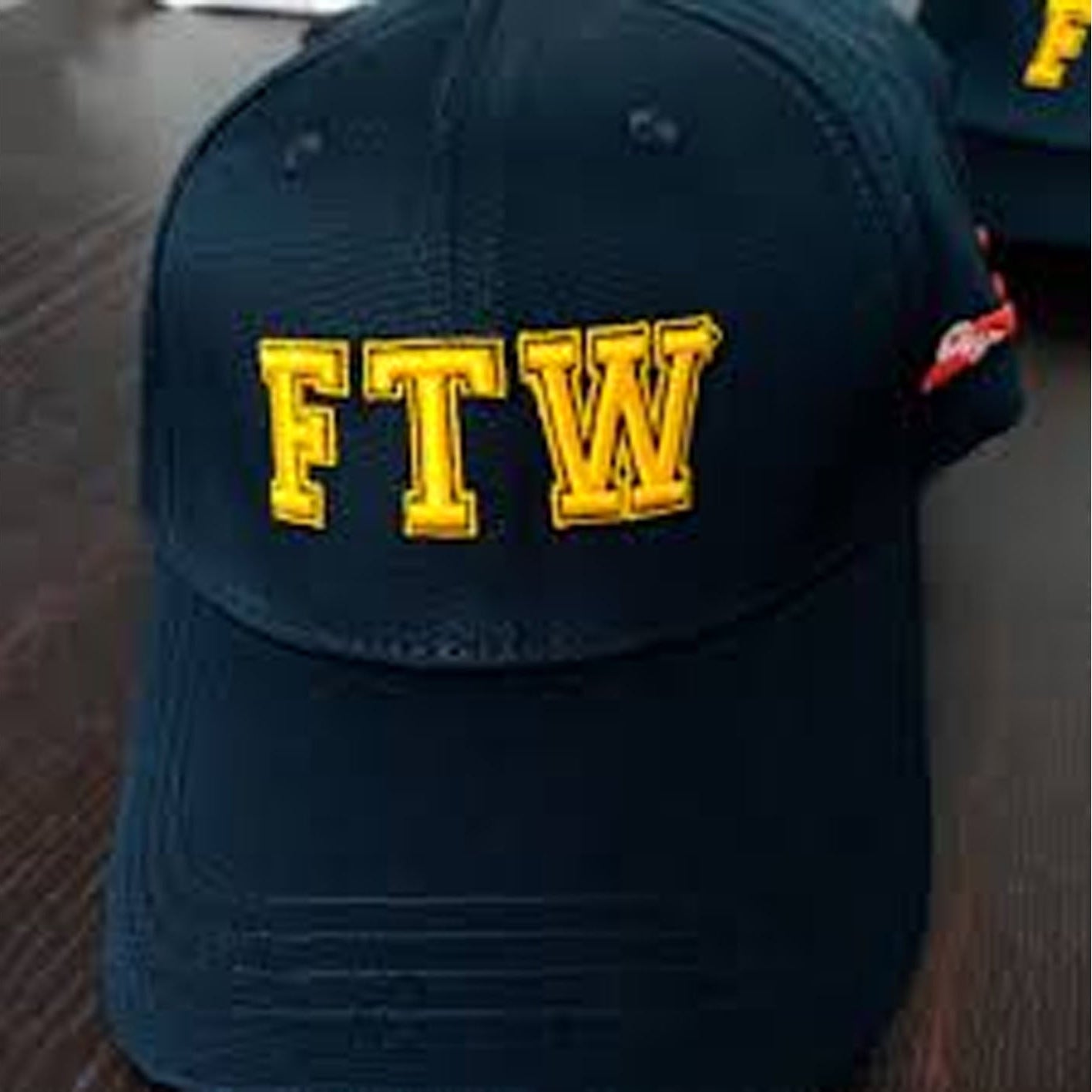 Navy blue cap with 'FTW' in yellow on a wooden surface