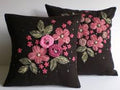 Two black pillows with pink floral embroidery on a white background