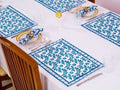 Table setting with blue and white patterned placemats on a white tablecloth.