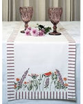 Table setting with a floral table runner, pink goblets, and flowers on a white tablecloth.