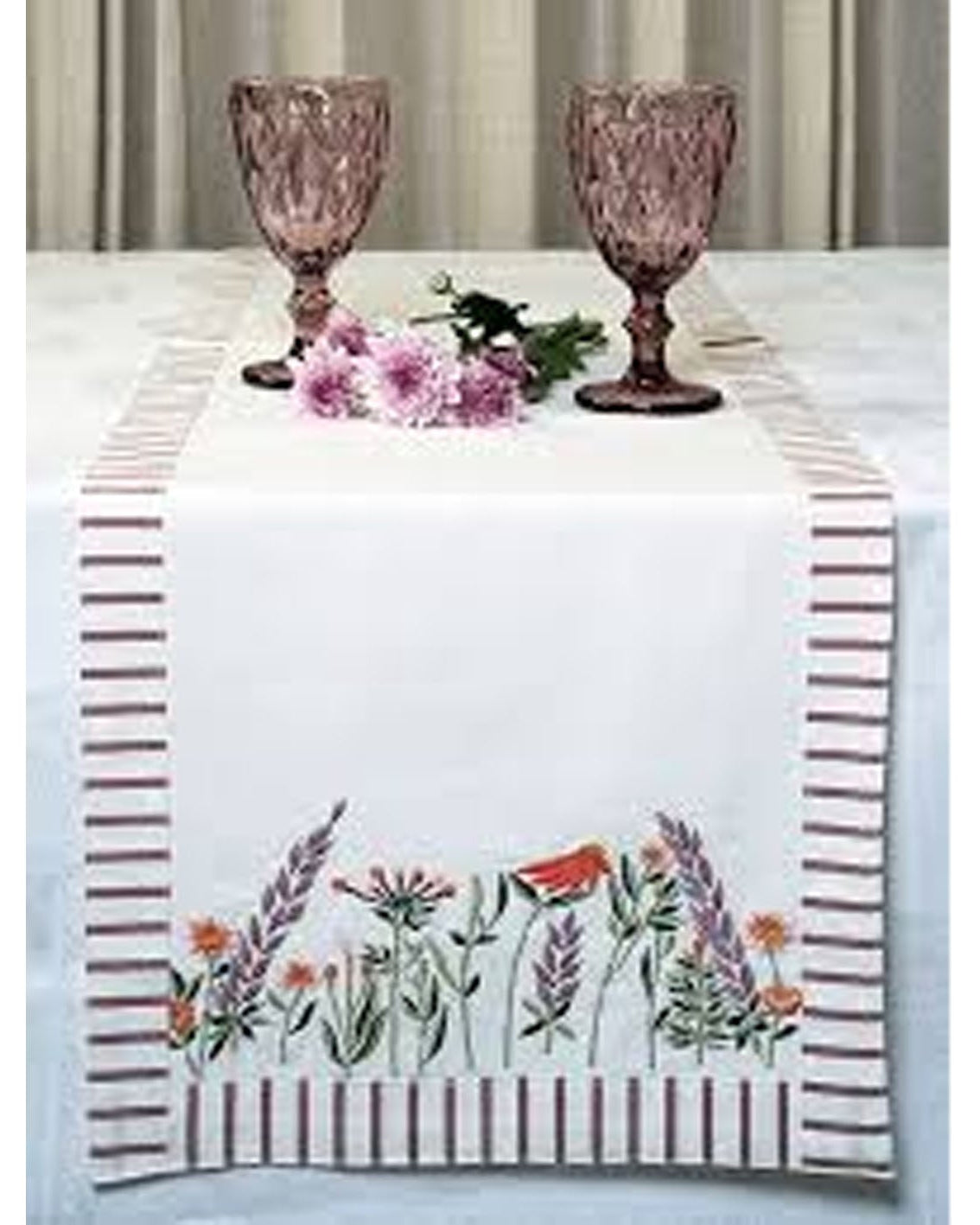 Table setting with a floral table runner, pink goblets, and flowers on a white tablecloth.