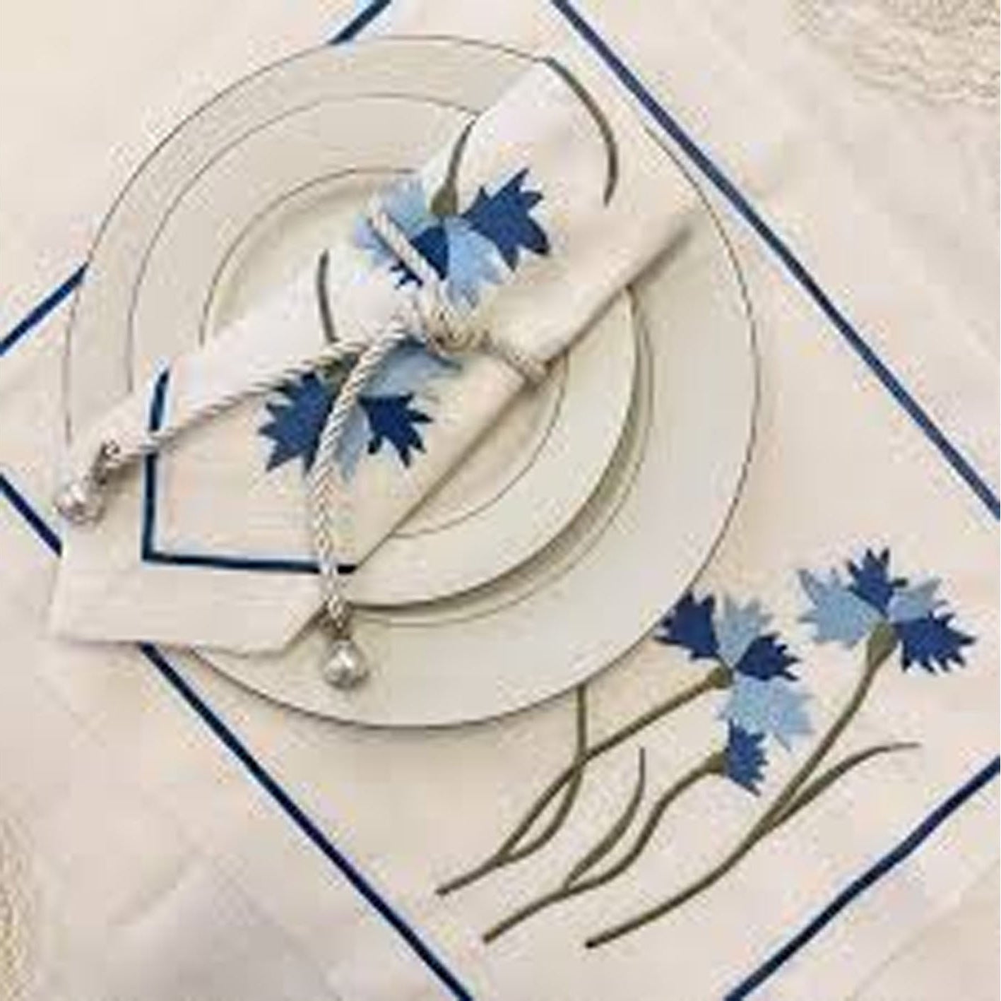 Decorative table setting with floral napkin and placemat on a white tablecloth.