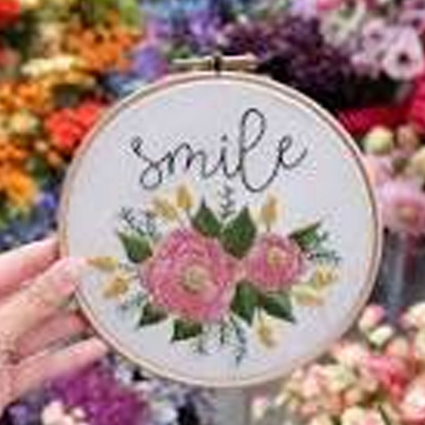 Embroidery hoop with floral design and 'smile' text held in front of a floral background