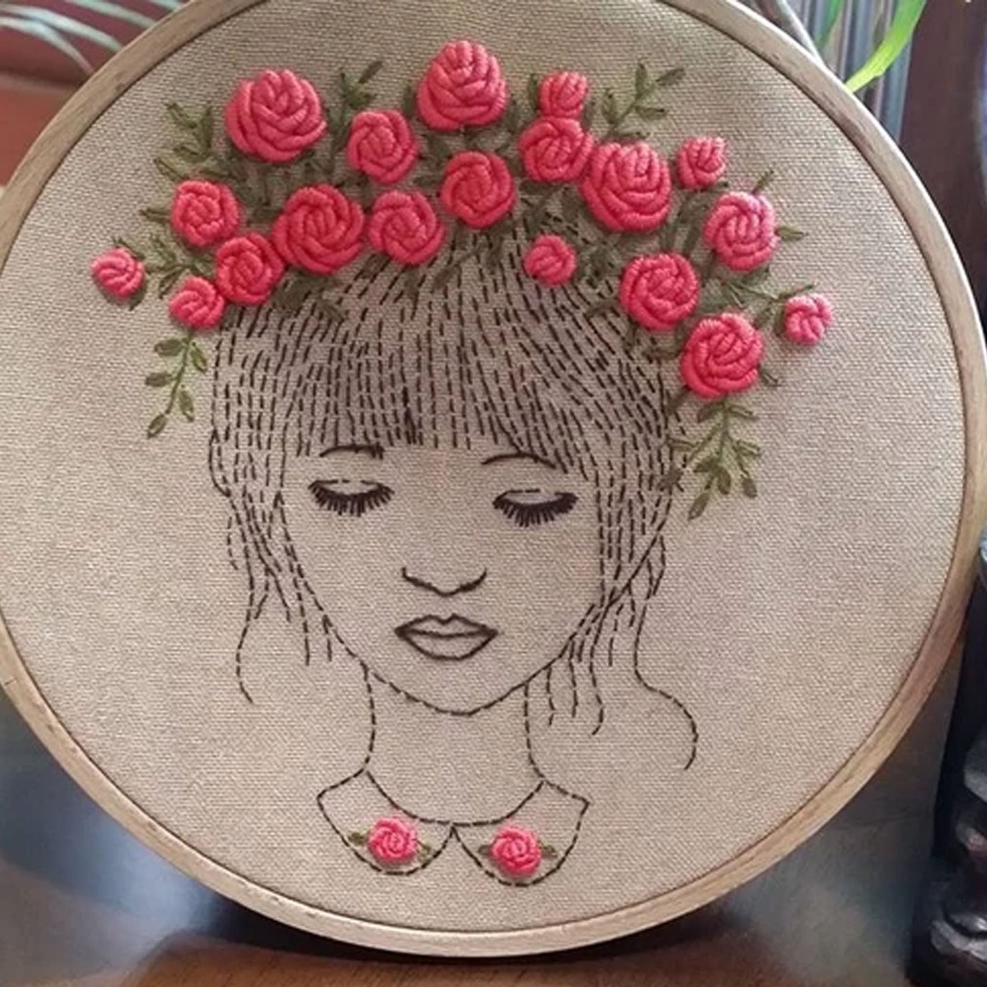 Embroidery hoop with a face design and pink flowers.