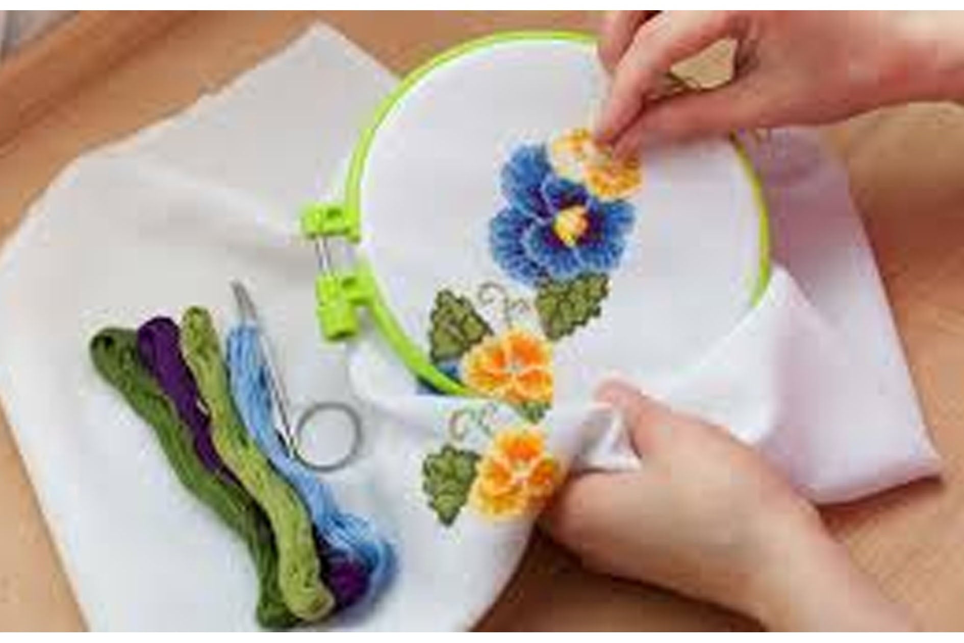 Embroidery hoop with floral design on fabric, surrounded by embroidery tools.