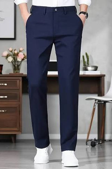A person wearing navy blue dress pants, a white shirt, and white sneakers, standing in a modern office setting with a desk, chair, and wooden cabinet in the background.