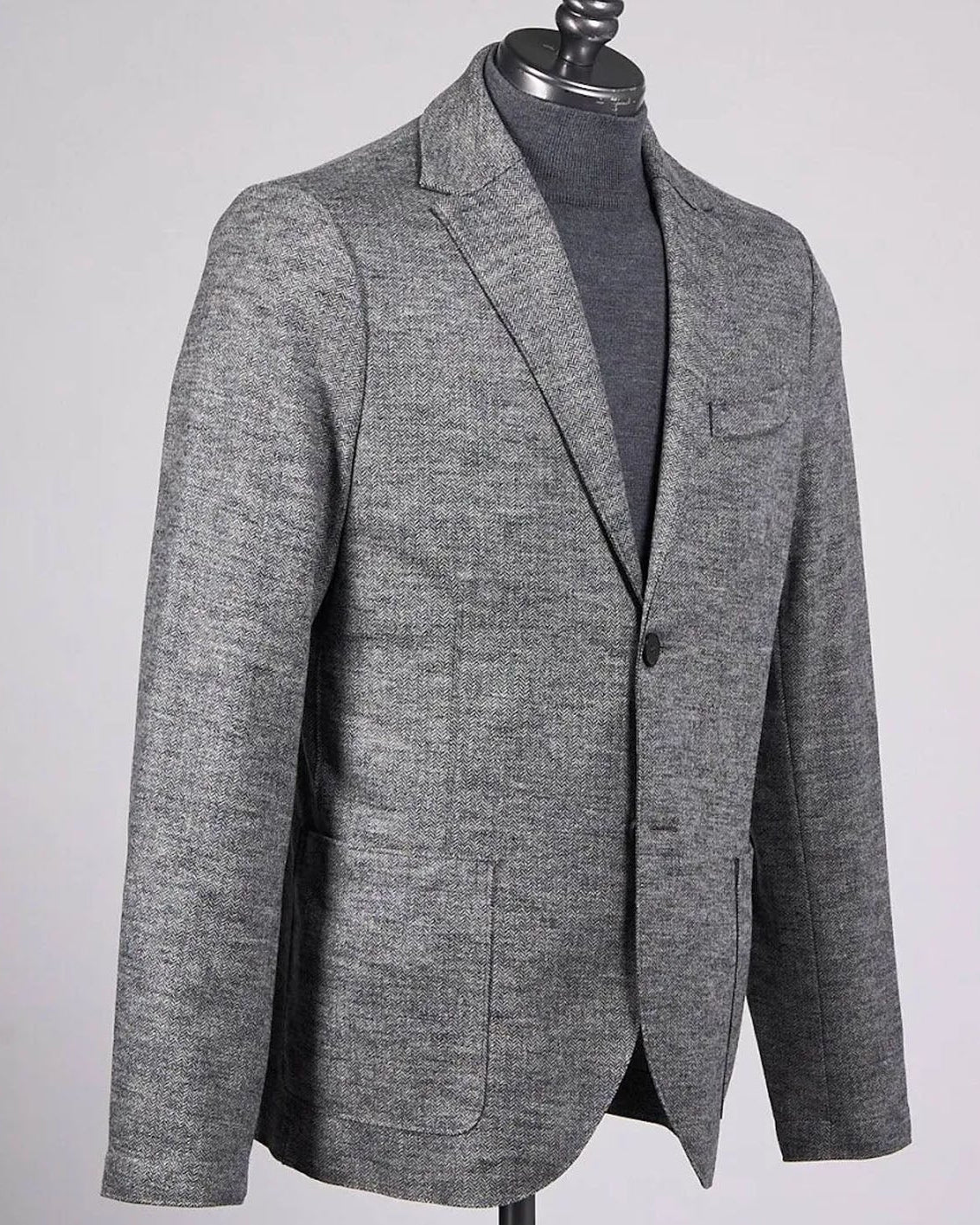A men's gray textured blazer displayed on a black mannequin torso, layered over a dark gray turtleneck sweater, against a light gray background.