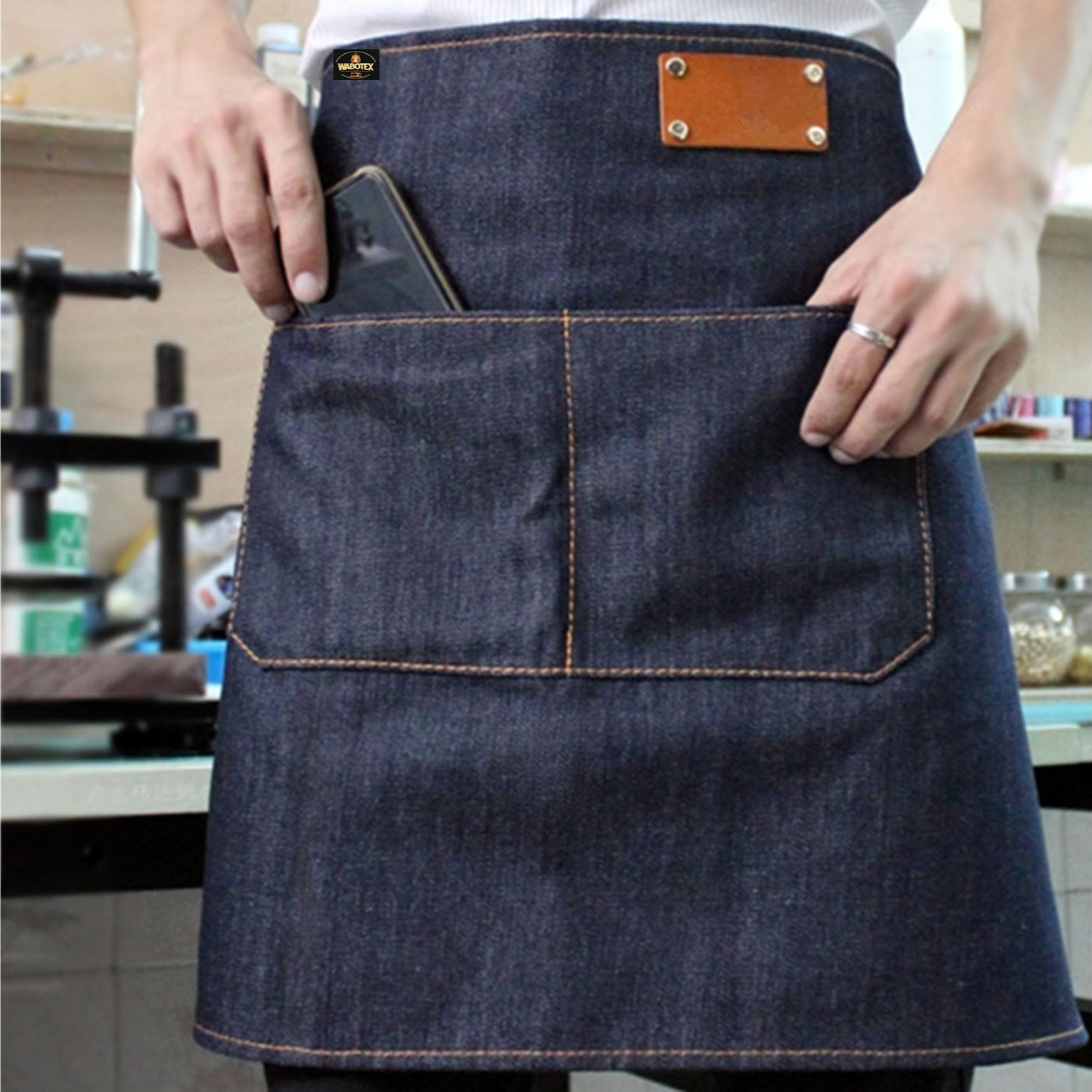 Person wearing a denim apron with a leather patch, holding a smartphone.