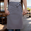 Person wearing a gray apron in an outdoor setting with wooden tables and chairs.