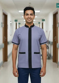 Man wearing a light purple uniform with black accents in a hospital corridor.
