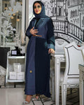 Woman in a blue abaya standing in a stylishly decorated room with architectural wall design.