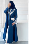 Woman wearing a blue abaya with white accents in a minimalistic setting