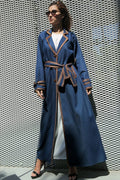Woman wearing a long blue coat with a patterned wall background