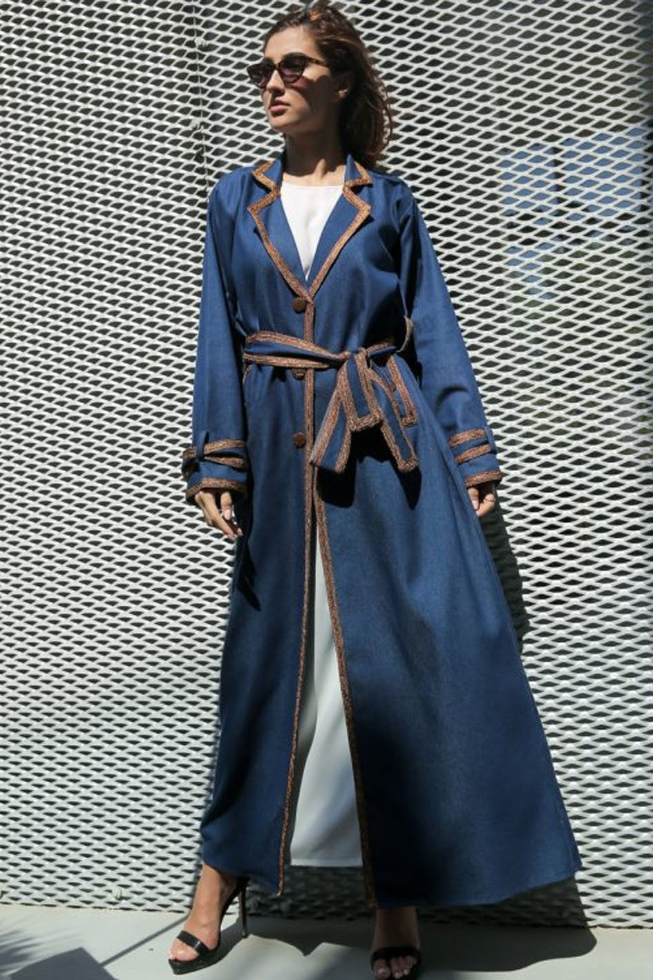 Woman wearing a long blue coat with a patterned wall background