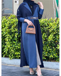 Woman in a blue dress holding a brown handbag with green bushes in the background