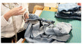 Person sorting through folded clothes on a table with a white background