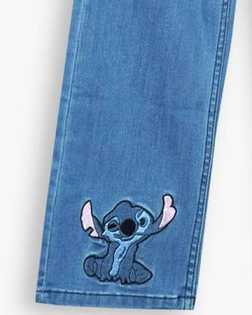 A close-up of a blue denim jeans leg featuring an embroidered patch of the cartoon character Stitch on the lower front.