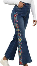 A person wearing dark blue flare jeans with colorful floral embroidery down the outer side of each leg, paired with a white long-sleeve top and white sneakers, shown against a plain white background.