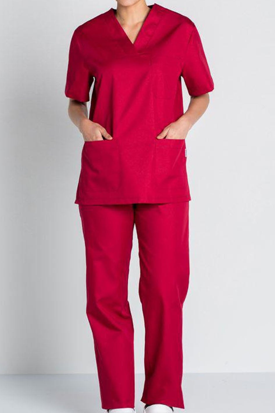 A model wearing a matching medical scrub set in a vibrant magenta pink, featuring a short-sleeve V-neck top with front pockets and matching straight-leg pants, shown against a light gray studio background.