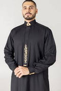 Man wearing a black traditional outfit with gold embroidery on a light gray background