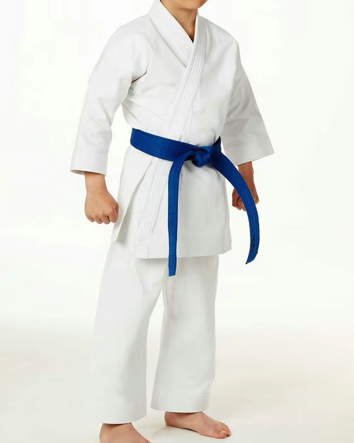 A child wearing a white martial arts gi with a bright blue belt, standing barefoot against a plain white studio background.