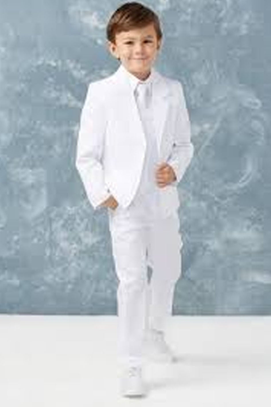 Young boy in a white suit standing against a light gray background