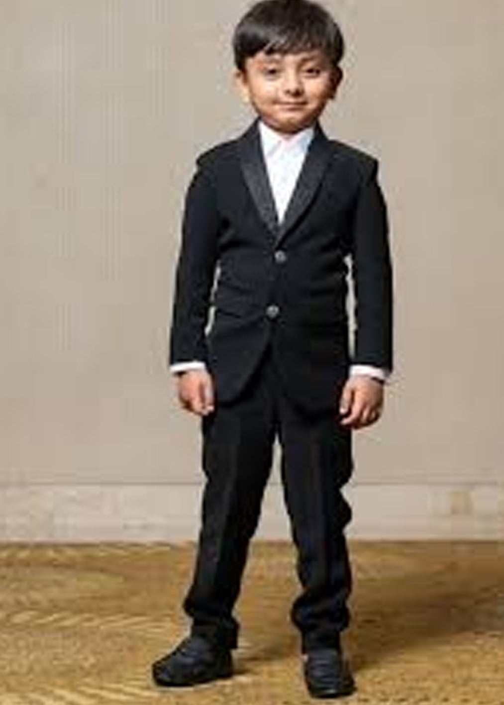 Child wearing a formal black suit against a neutral background