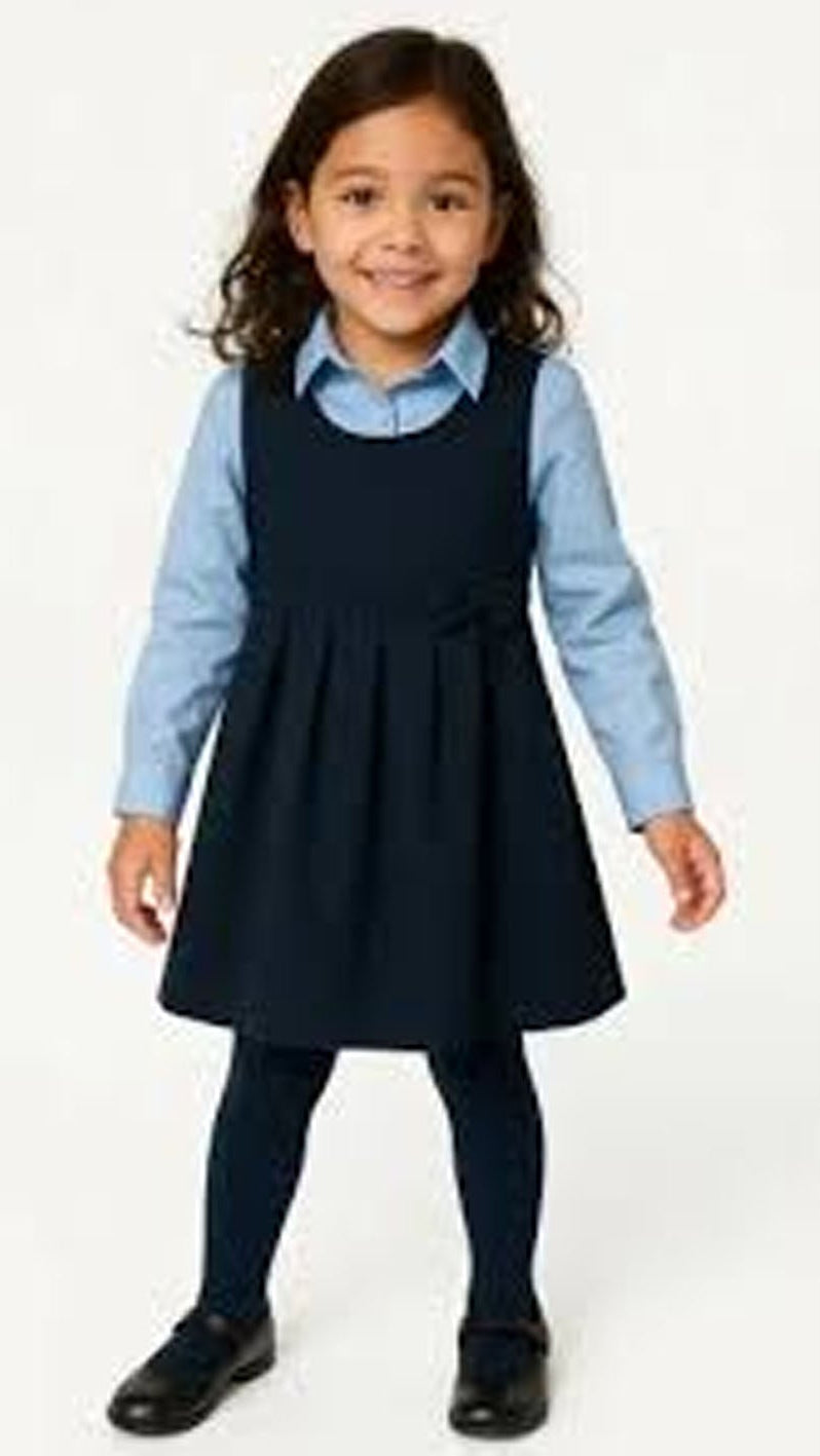 Young girl wearing a navy pinafore dress over a light blue shirt on a white background