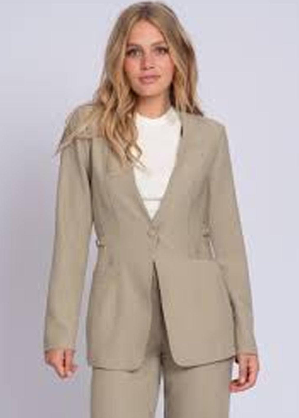 Woman wearing a beige suit with a white shirt on a light gray background