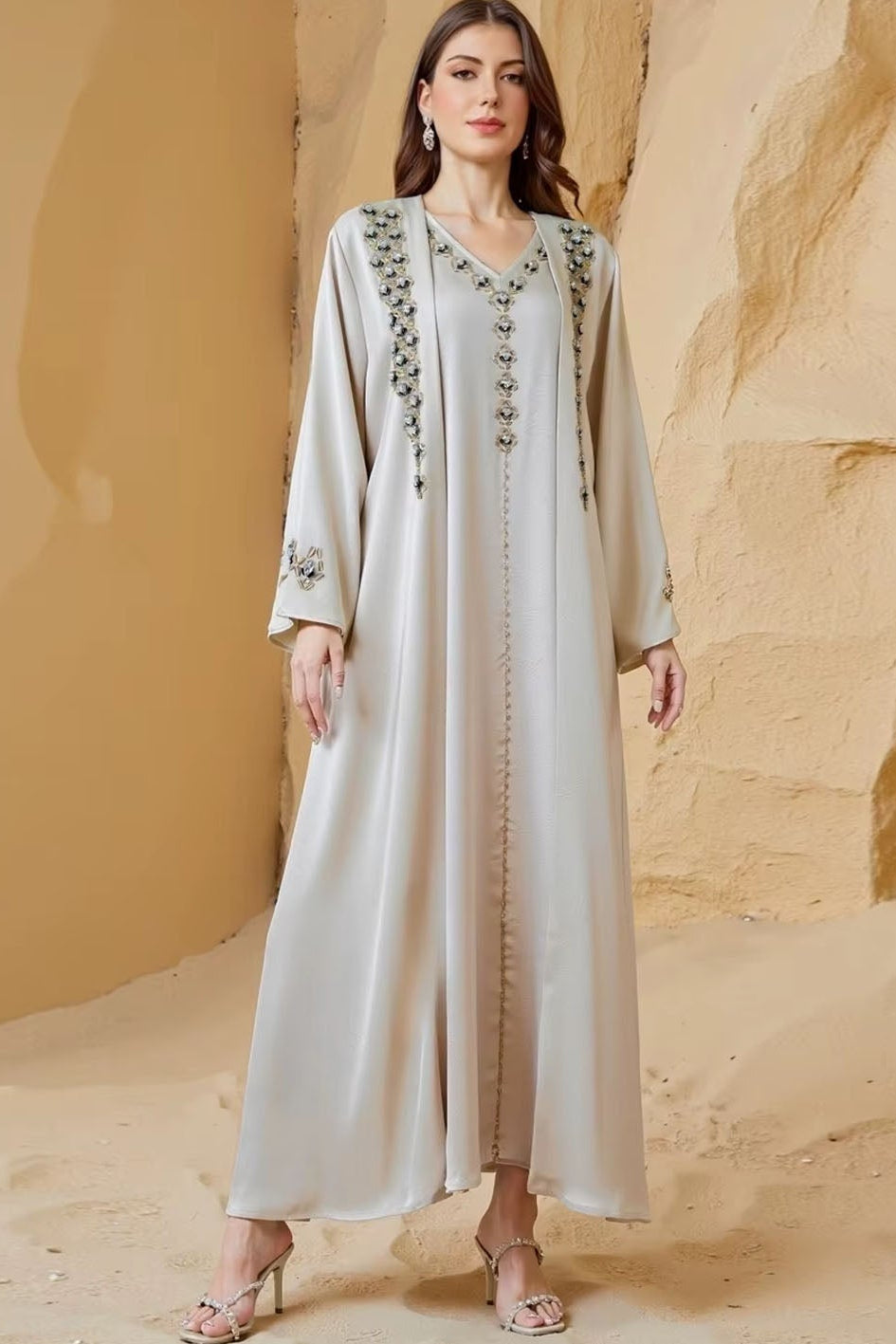 Woman wearing a long, light-colored dress with intricate patterns against a beige wall.