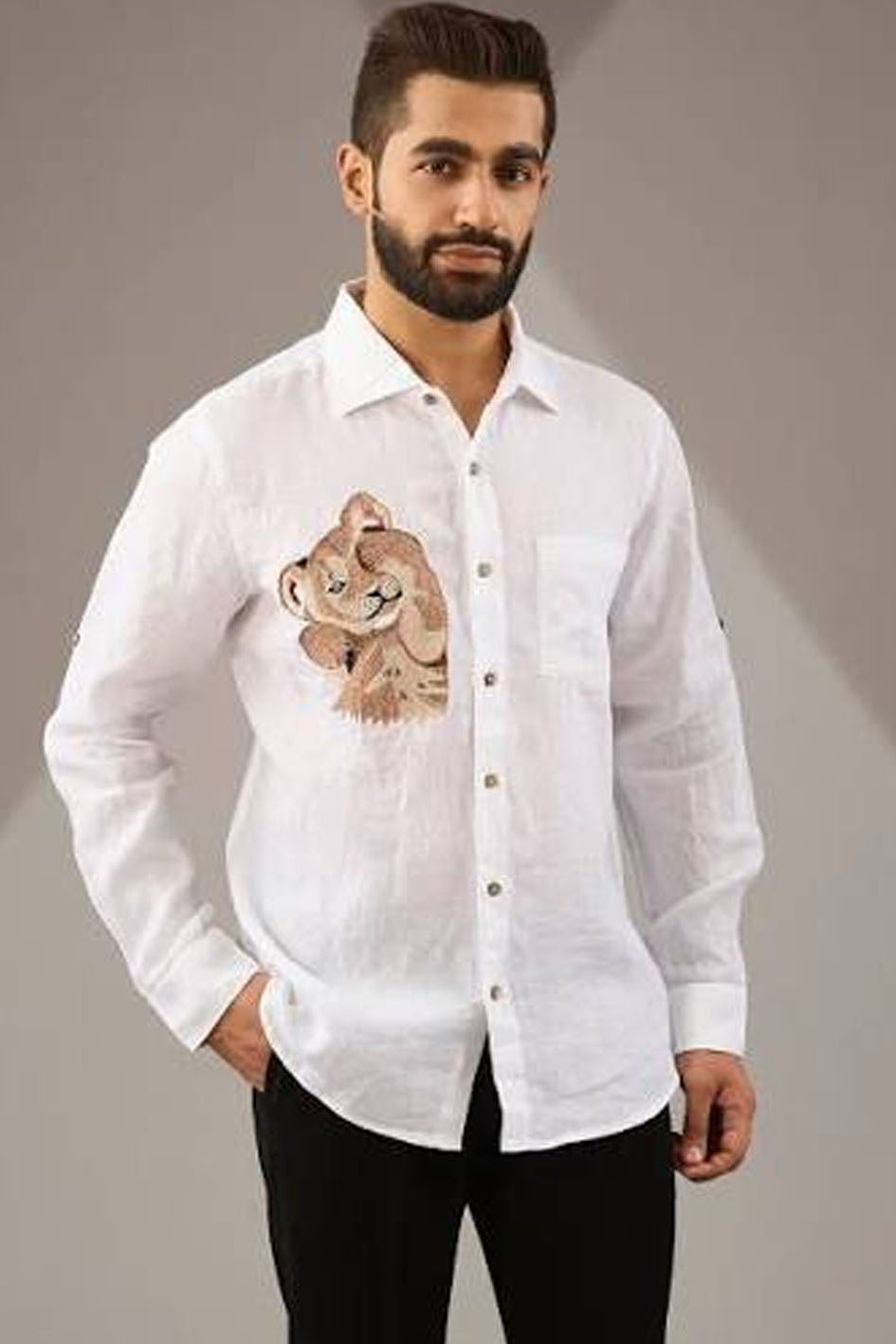 A man weraing a white linen shirt with a bear embroidered
