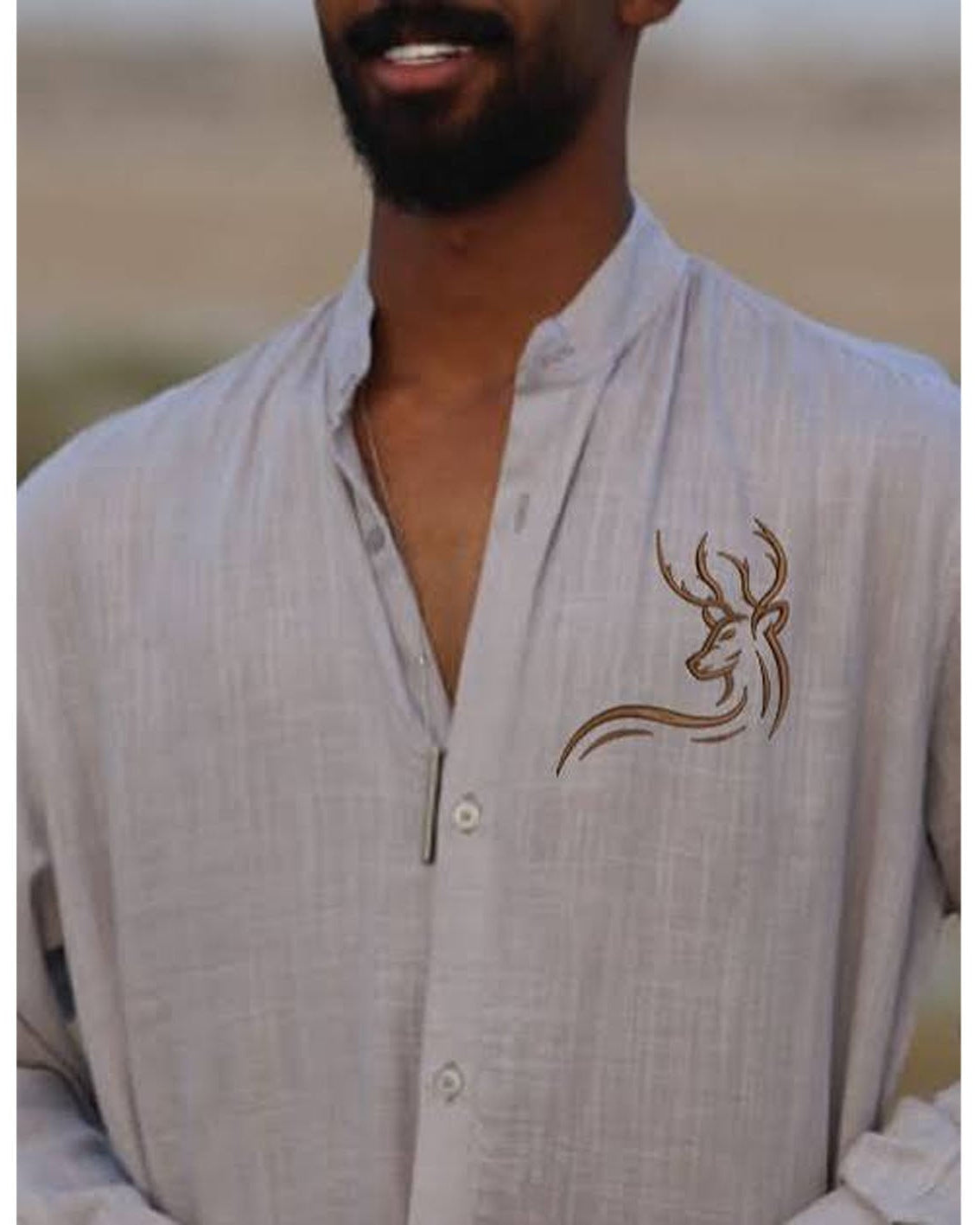 A man wearing a grey linen shirt with a deer logo embroidered